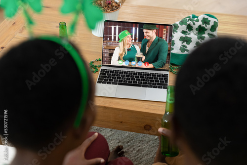 African american couple making st patrick's day video call to friends on laptop at home