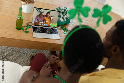 African american couple making st patrick's day video call to happy male friends on laptop at home