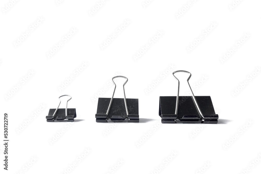 Three black binder clips of various sizes used to staple documents against Three black binder clips of various sizes used to staple documents against