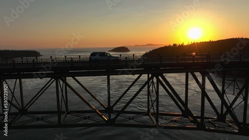 Drone shot of an SUV driving through the sunset's glow on Deception Pass. photo