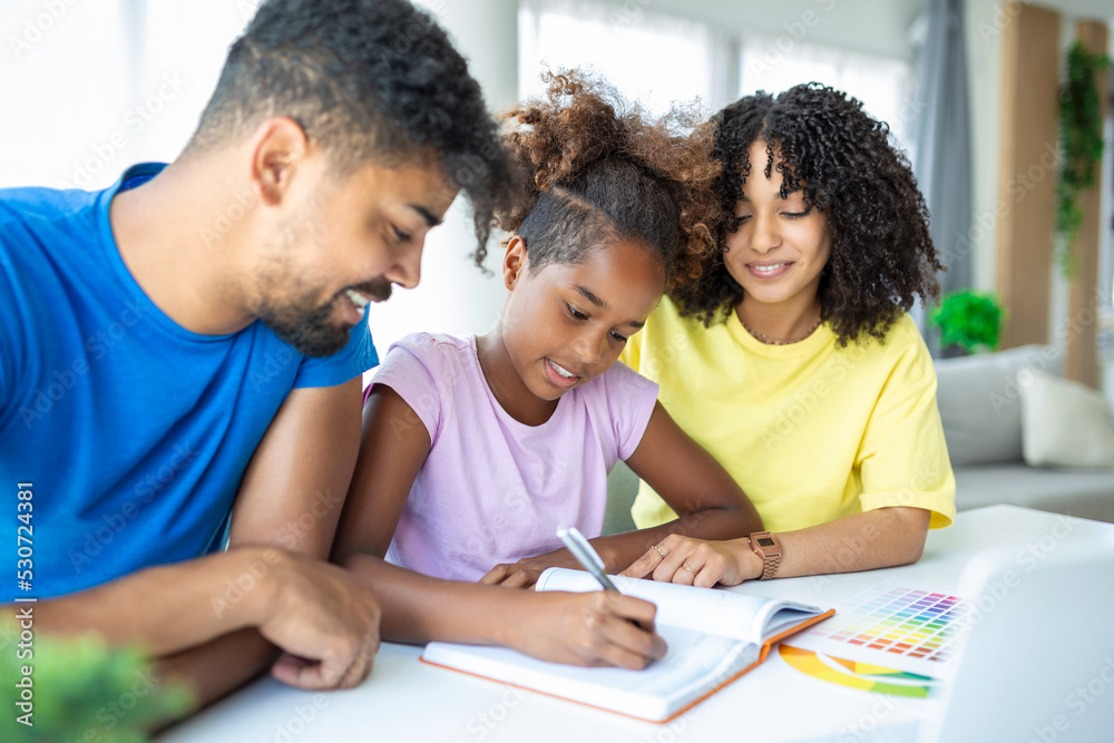 A mixed race husband and wife doing homework with their daughter while social distancing and isolating at home during the Covid-19 pandemic. A mixed race husband and wife doing homework with their daughter while social distancing and isolating at home during the Covid-19 pandemic.