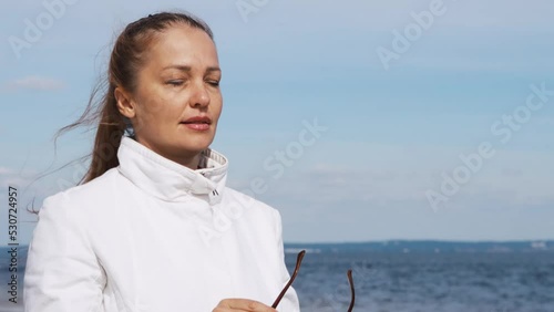 a beautiful woman with red hair in a white coat walks on a sandy beach on a cold sunny day, the unity of woman and nature