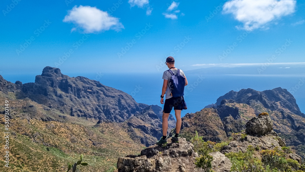 Man with backpack enjoying panoramic view on the Teno mountain massif seen from summit Pico Verde, Tenerife, Canary Islands, Spain, Europe. Hiking trail between Masca and Santiago. Wanderlust vibe