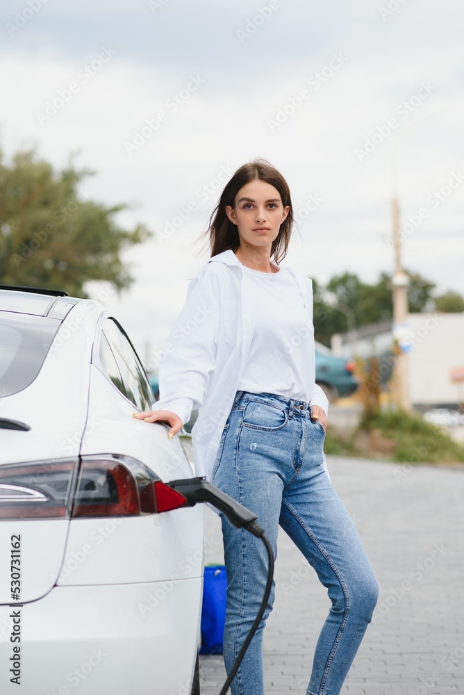 Woman near electric car. Vehicle charged at the charging station.