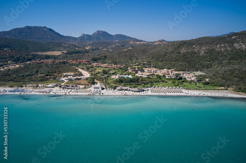 Sardinia panorama clear water aerial view. Sardinia famous beaches white sand clear turquoise water aerial view. The beaches of Sardinia in the background mountains cumulus clouds top view.