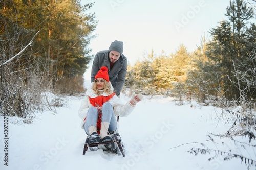 Young happy couple sledding in winter at forest