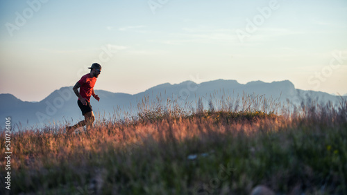 A young sportsman runs at sunset in the hills