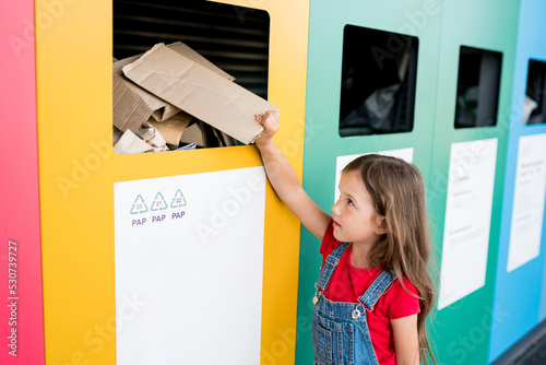 Girl recycling cardboard in paper bank. Children putting papers in recycling bin. Sustainble lifestyle concept.