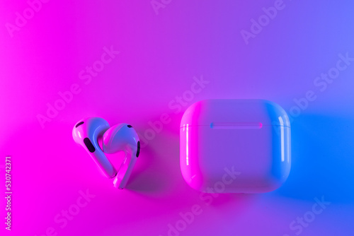 White modern headphones wireless earphones with case, copy space neon pink and blue background