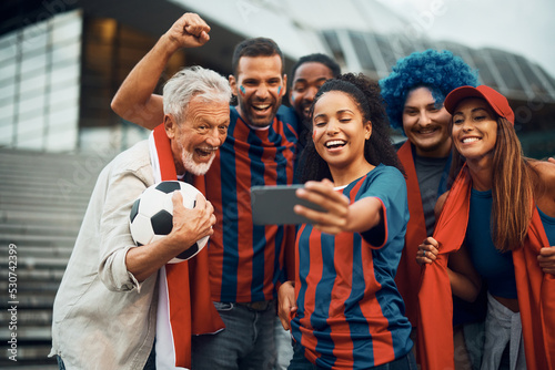 Cheerful soccer fans have fun while taking selfie with cell phone.