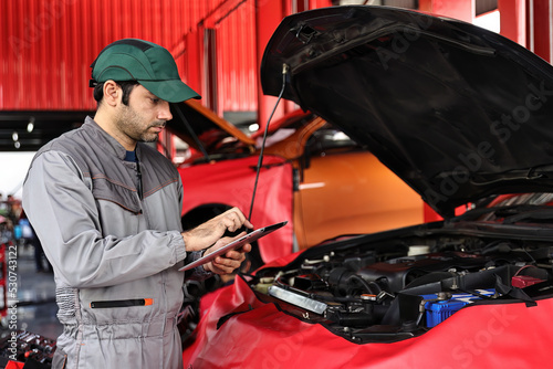 Car mechanic working with a laptop in Auto Repair Service checking car engine