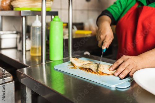 Fototapeta Naklejka Na Ścianę i Meble -  Worker slicing a piece of mexican taco in a kitchen of a restaurant