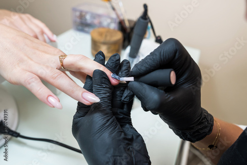 Close-up of a manicurist making a pale pink manicure on a young woman's hand. Manicurist woman doing nails to a client girl in a beauty salon.