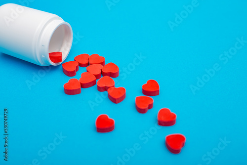 Red heart shaped pills with plastic bottle on blue background.Concept love addiction, love drugs, Valentine's Day and depression © SNAB
