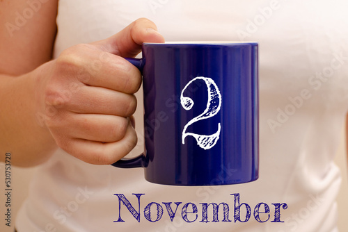 The inscription on the blue cup 2 november. Cup in female hand, business concept