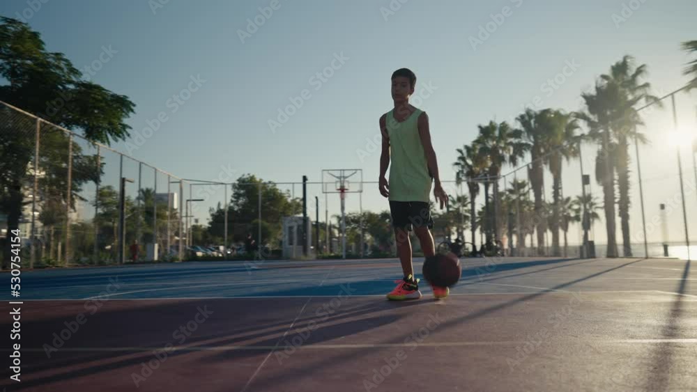12 year old boy bouncing basketball ball training on ground floor of the court. Basketball player. Workout. Sport activities. High quality 4k footage