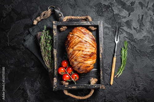 Roast bacon wrapped meatloaf, meat loaf in a tray with herbs. Black background. Top view photo