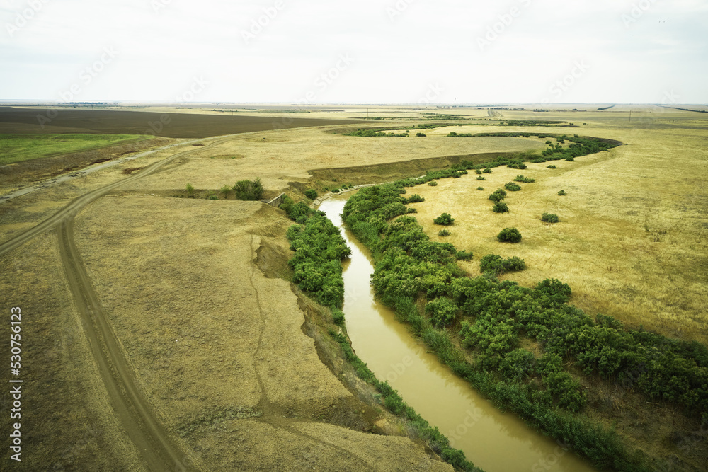 Naklejka premium a winding muddy river with overgrown green banks in a sun-scorched steppe rural landscape