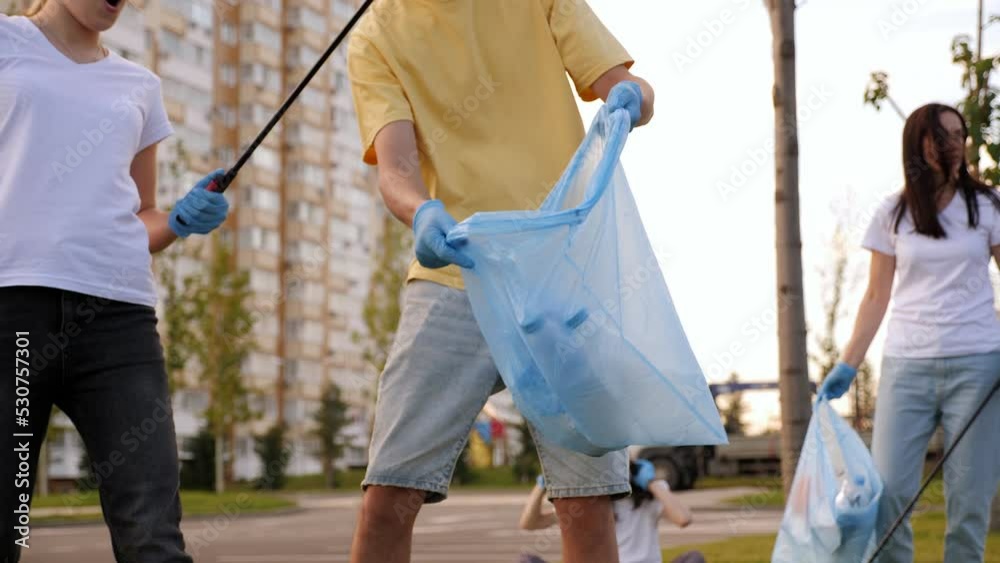 Close-up of volunteers with gloves and forceps collecting plastic waste in urban development. The girl collects banana peelings and plastic bottles in a bag. Close-up of volunteers with gloves and forceps collecting plastic waste in urban development. The girl collects banana peelings and plastic bottles in a bag.