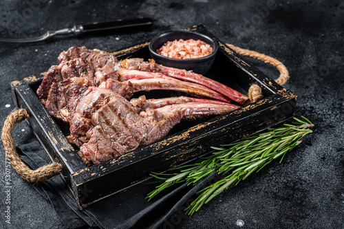 Grilled lamb chop steak, mutton meat cutlet in wooden tray. Black background. Top view