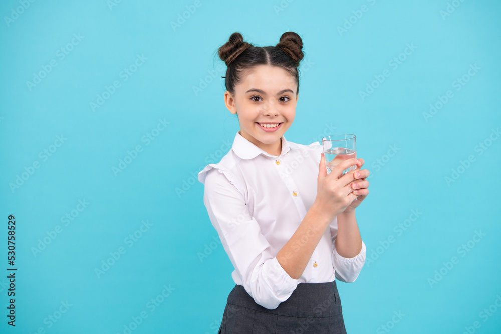 Teenager girl drinking water from glass on blue background. Daily life health. Drink water for health care and body balance. Thirsty kid, dehydration. Happy teenager, positive and smiling. Teenager girl drinking water from glass on blue background. Daily life health. Drink water for health care and body balance. Thirsty kid, dehydration. Happy teenager, positive and smiling.