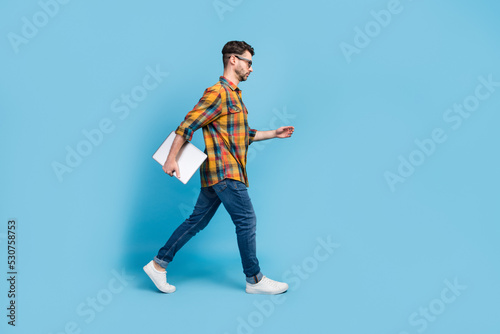 Full size profile portrait of serious confident person hold netbook walk empty space isolated on blue color background