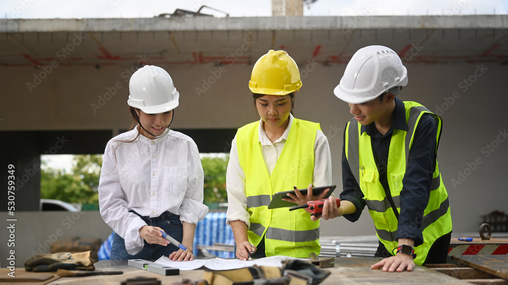 Architect team in safety helmet using digital tablet and working with blueprints during inspecting construction site Architect team in safety helmet using digital tablet and working with blueprints during inspecting construction site