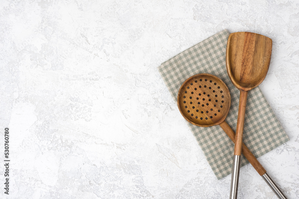 Cooking spoon and skimmer over kitchen towel on stone table Cooking spoon and skimmer over kitchen towel on stone table