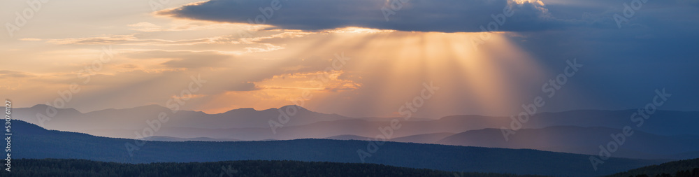 Picturesque sunset in the mountains, sun rays through the clouds