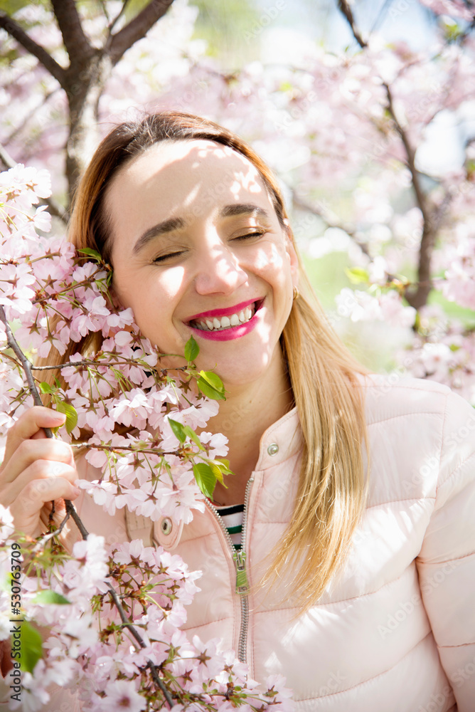 portrait of a smiling blonde woman with closed eyes in spring park in pink blossoming sakura portrait of a smiling blonde woman with closed eyes in spring park in pink blossoming sakura