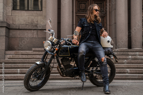 Portrait of guy looking like macho posing with motorbike outdoors.