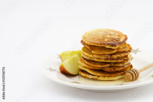 Stack of pancakes with apple slices and honey on the plate isolated on white background