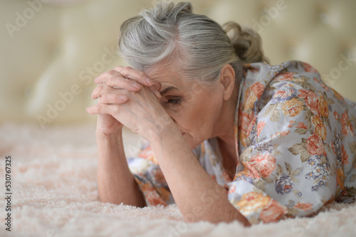 Thoughtful nice senior woman lying on bed