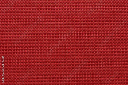 An extreme close-up of the cover of a vibrant rich red hardback book showing the pattern of dimples and nodules all in rows, flat, vertical and parallel to camera