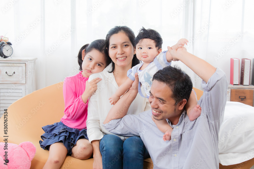 Selective focus Asian happy family laughing and hugging with love and warmth, smiling parents and eldest sister with toddler having fun together in holiday, family enjoying free time. Selective focus Asian happy family laughing and hugging with love and warmth, smiling parents and eldest sister with toddler having fun together in holiday, family enjoying free time.