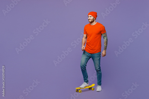 Full body side view fun happy young european man 20s he wear red hat t-shirt riding pennyboard skateboard isolated on plain pastel light purple background studio portrait. People lifestyle concept.
