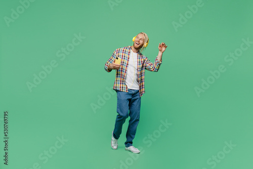 Young blond man blond man with dreadlocks 20s wear casual shirt headphones listen music use mobile cell phone isolated on pastel plain light green background studio portrait. People lifestyle concept.