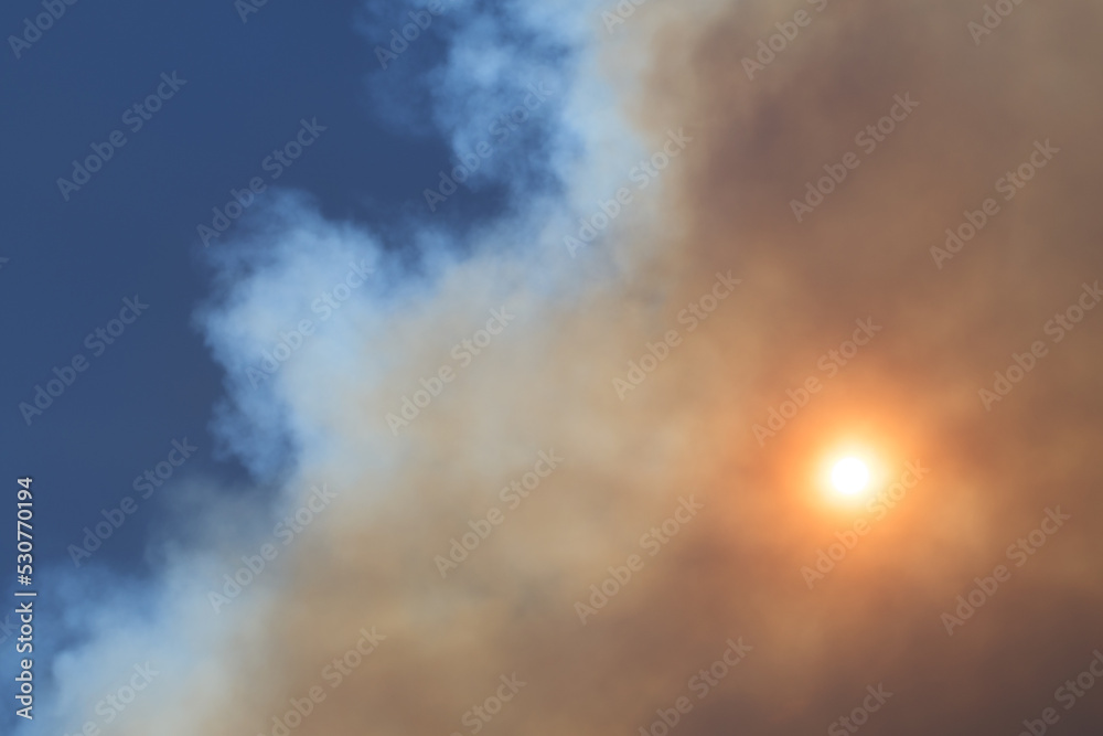 Sun obscured by a cloud of wildfire smoke, blue sky in background