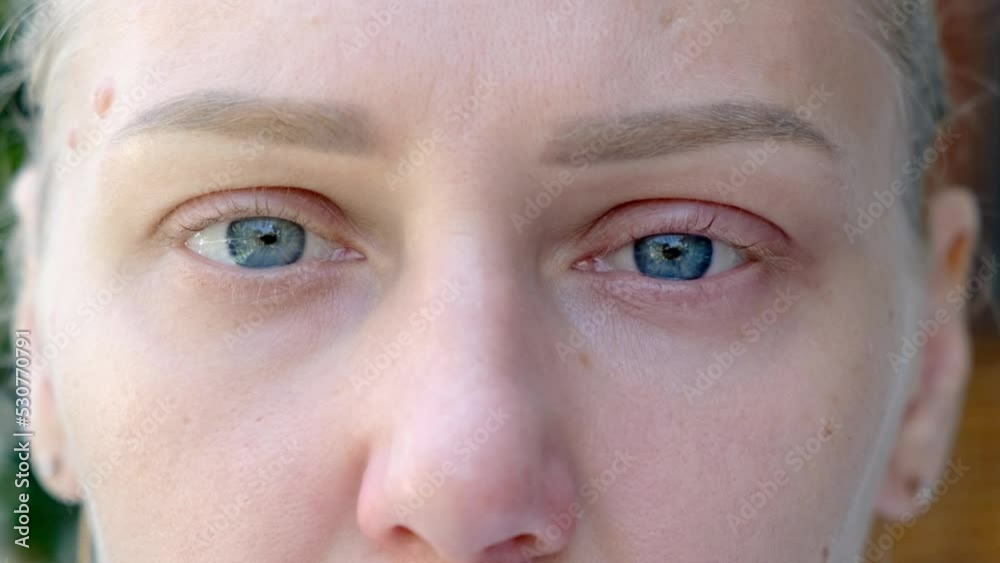 Close-up of macro zoom shot of sad wet blue eyes. Young beautiful blonde looks into the camera. Eyes of a girl with long beautiful eyelashes. Close-up of caucasian woman with sad look