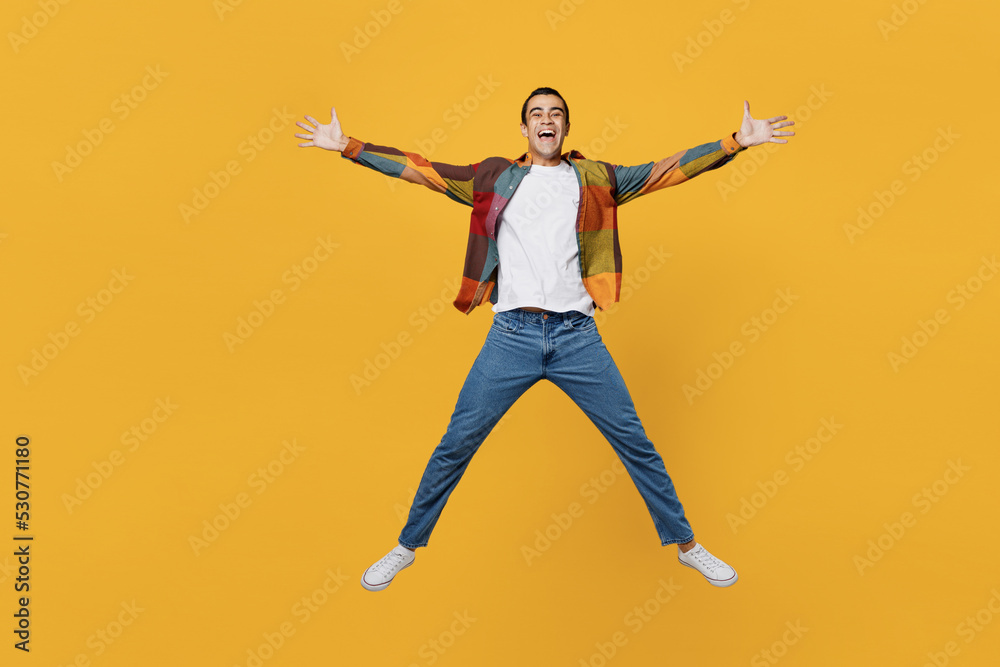 Full size young carefree middle eastern man wear casual shirt white t-shirt jump high with outstretched hands like flying isolated on plain yellow background studio portrait People lifestyle concept.
