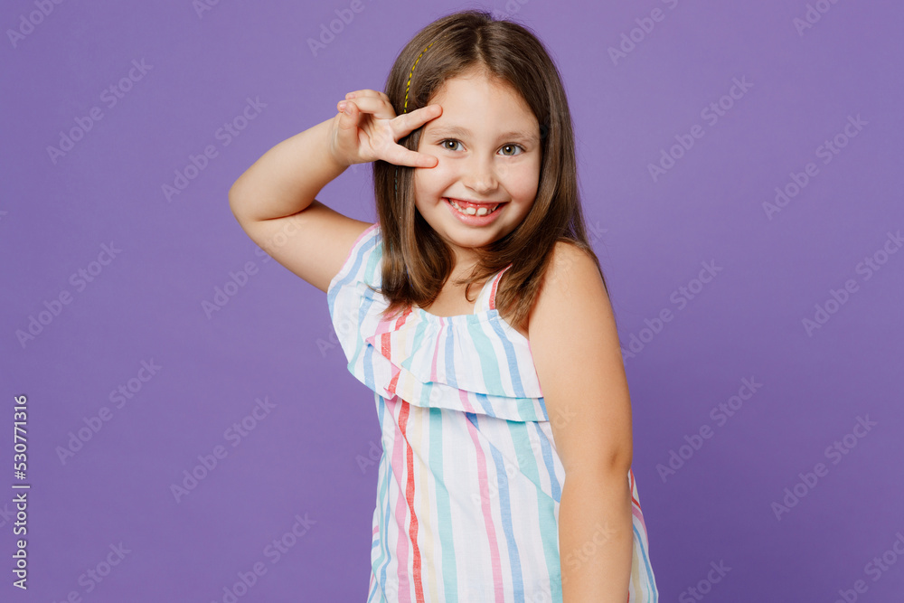 Little smiling happy fun cool kid child girl 5-6 years old wears striped dress cover eye with victory sign isolated on plain pastel light purple background. Mother's Day love family lifestyle concept. Little smiling happy fun cool kid child girl 5-6 years old wears striped dress cover eye with victory sign isolated on plain pastel light purple background. Mother's Day love family lifestyle concept.