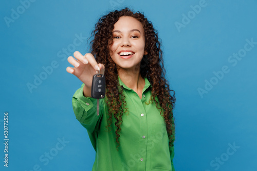 Young cheerful fun happy woman of African American ethnicity 20s she wear green shirt hold give car keys fob keyless system isolated on plain blue background studio portrait. People lifestyle concept.
