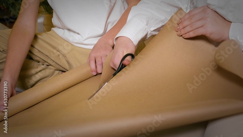 A joyful teenage girl and her younger brother create gift boxes with Christmas gifts at home.