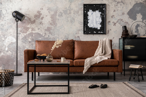 Interior design of loft industrial apartment with mock up poster frame, brown sofa, coffee table and black commode and personal accessories. Concrete gray wall. Home decor. Template. photo