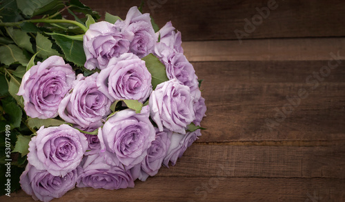 a bouquet of delicate purple roses on a background of dark wooden boards with a copy of the space © Irina