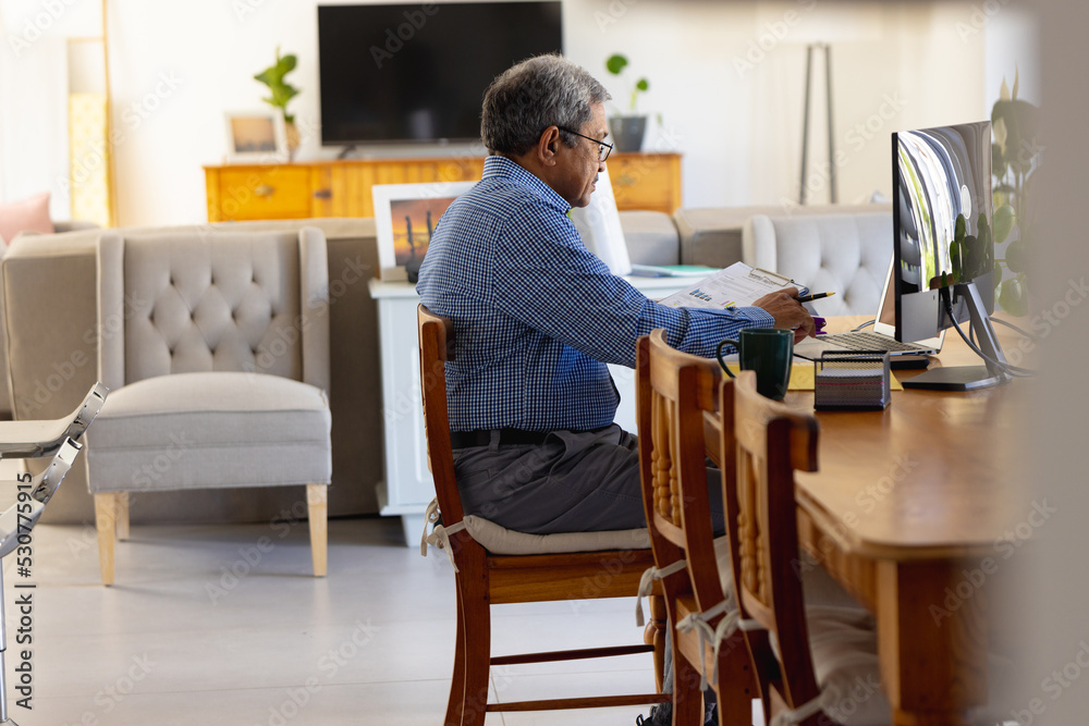 Senior biracial businessman using computer sitting at desk at home Senior biracial businessman using computer sitting at desk at home
