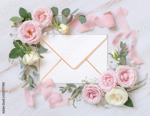 Blank envelope between pink roses and pink silk ribbons top view, wedding mockup
