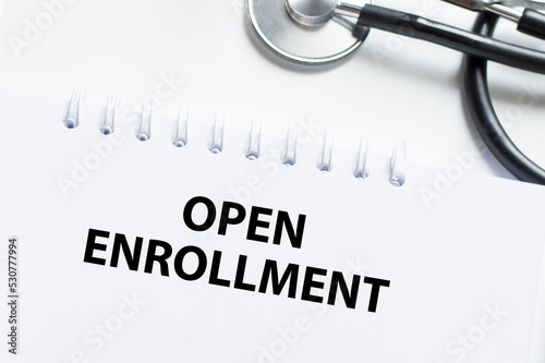OPEN ENROLLMENT text on a notebook next to a stethoscope on a light desk. Medical concept.
