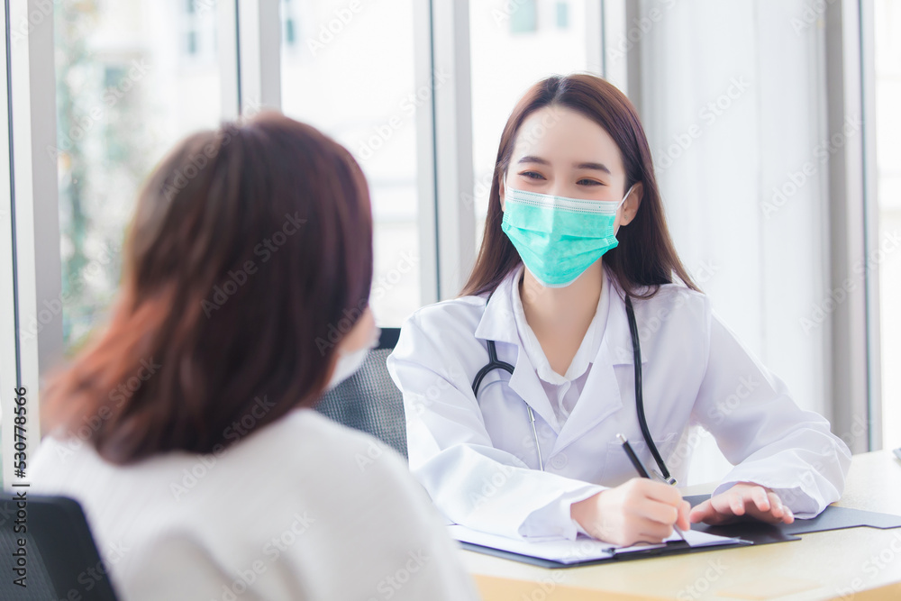 Asian elder female consults with professional woman doctor about her symptom or health problem while she wears medical face mask in examination room at hospital at health care concept. Asian elder female consults with professional woman doctor about her symptom or health problem while she wears medical face mask in examination room at hospital at health care concept.