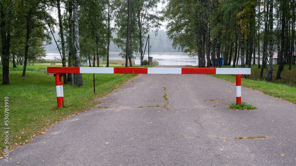 Entry is prohibited. Red and white barrier on the road. The road leads to the lake